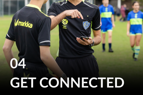 Two young male referees are on the field. One is pointing to his mobile phone.